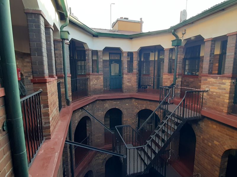 An exterior view of an apartment building courtyard featuring exposed brickwork, arched entryways, and a central metal staircase with wrought iron railings.