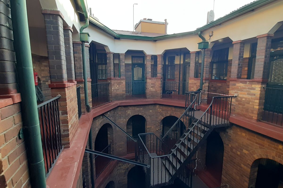 An exterior view of an apartment building courtyard featuring exposed brickwork, arched entryways, and a central metal staircase with wrought iron railings.