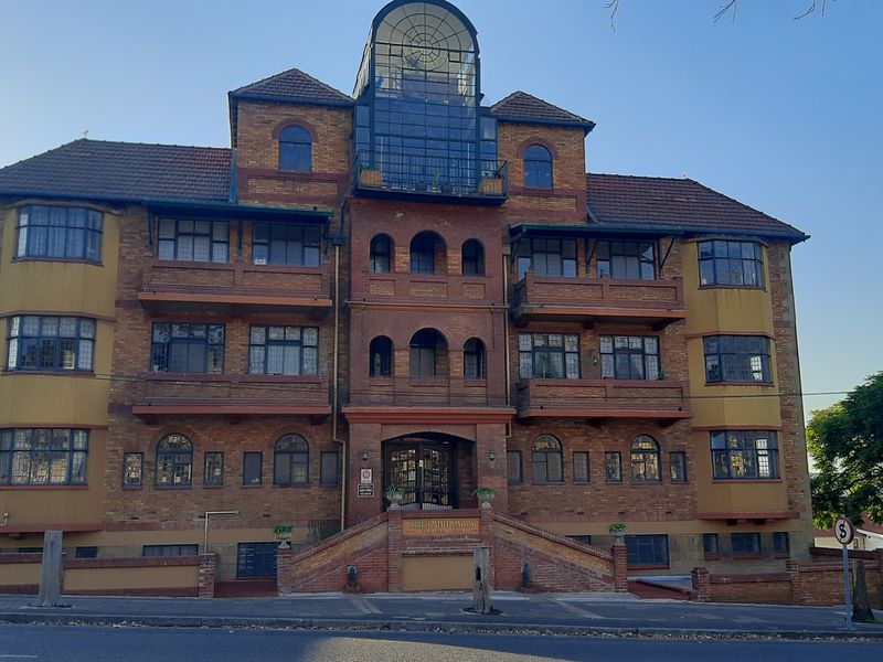 Front elevation of a multi-story brick apartment building featuring arched windows, private balconies, and a prominent glass atrium structure.