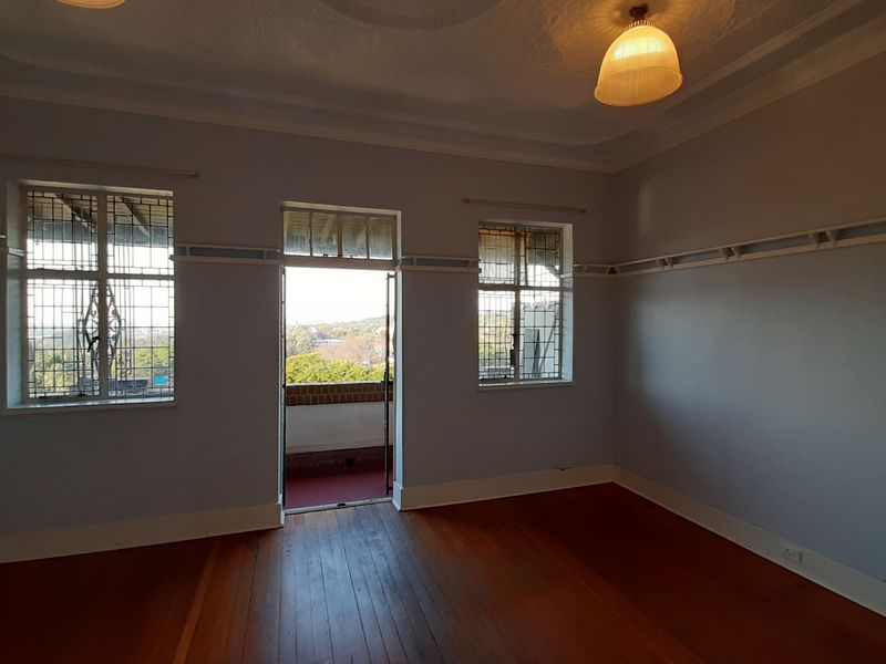A spacious, empty bedroom featuring original hardwood flooring, decorative ceiling rose, picture rails, and direct access to a private balcony with security bars.