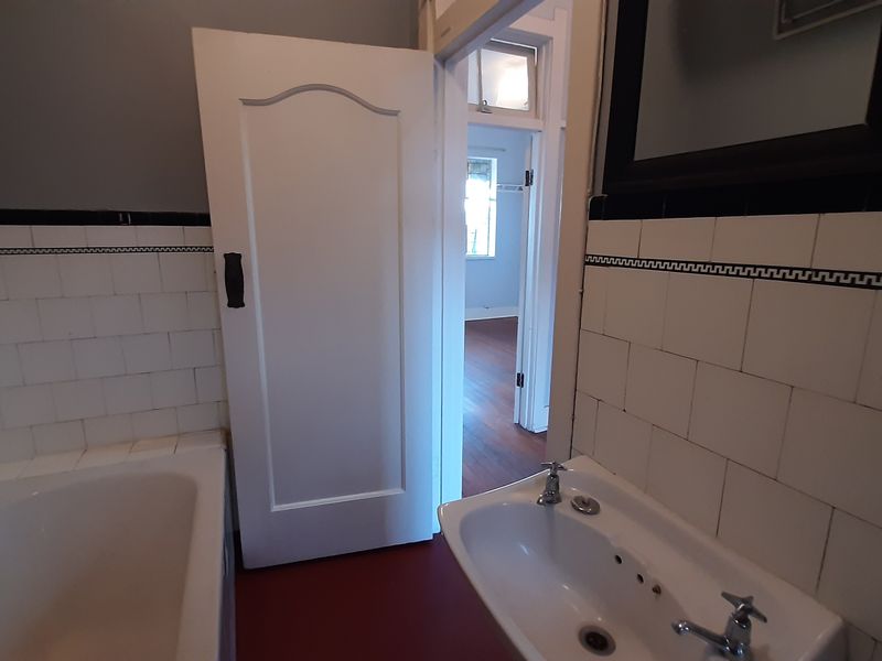 A dated bathroom featuring a built-in bathtub and wall-mounted basin with classic tiled splashbacks, requiring cosmetic updates to modernize the space.