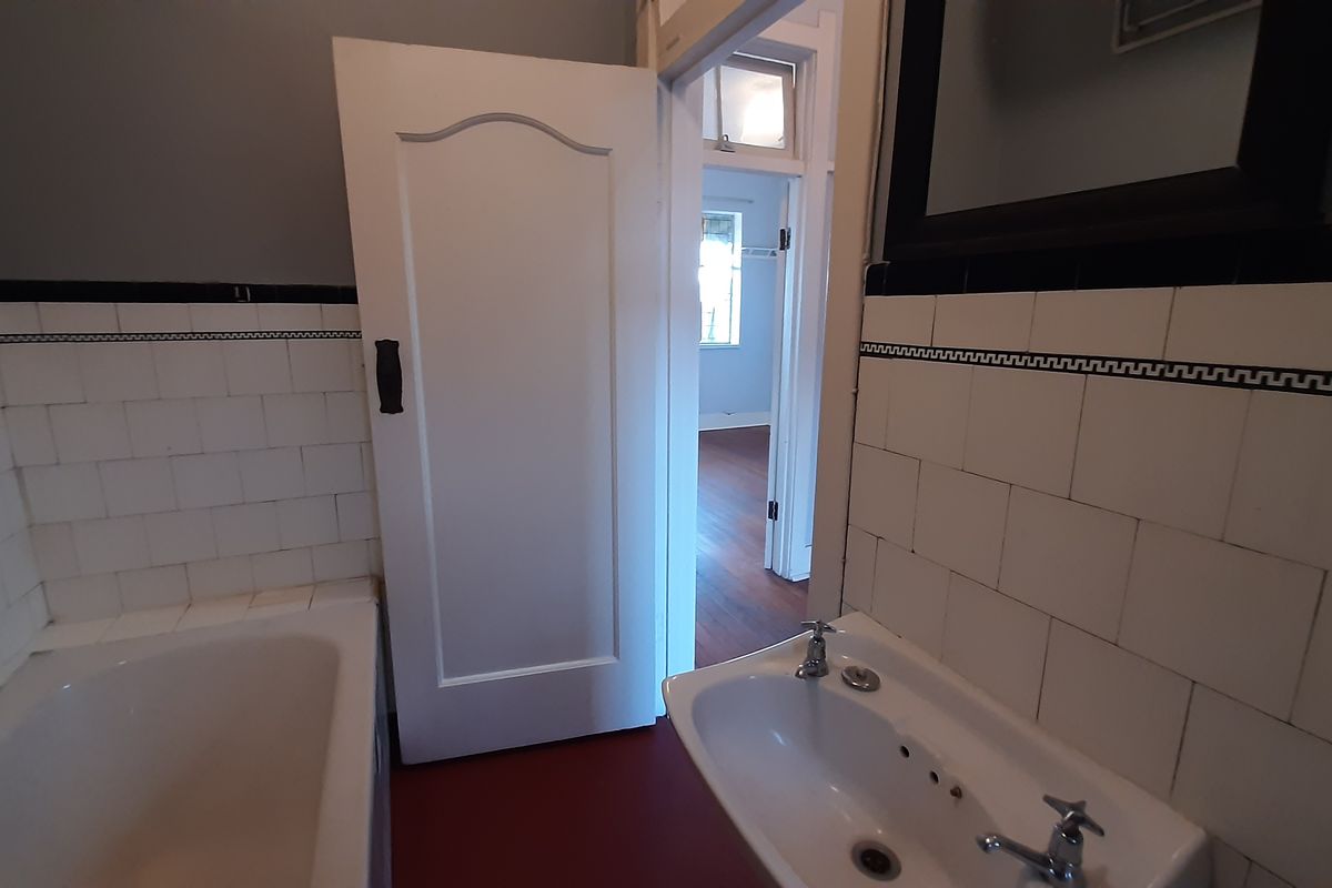 A dated bathroom featuring a built-in bathtub and wall-mounted basin with classic tiled splashbacks, requiring cosmetic updates to modernize the space.