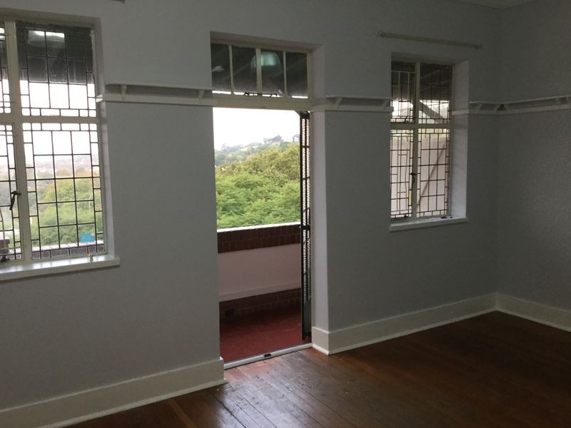 Spacious living area featuring original hardwood flooring, classic leaded glass windows, picture rails, and direct access to an outdoor balcony.