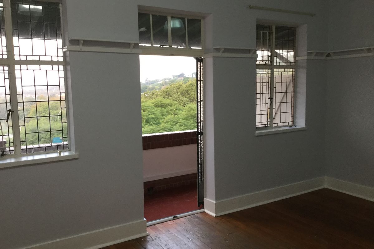 Spacious living area featuring original hardwood flooring, classic leaded glass windows, picture rails, and direct access to an outdoor balcony.