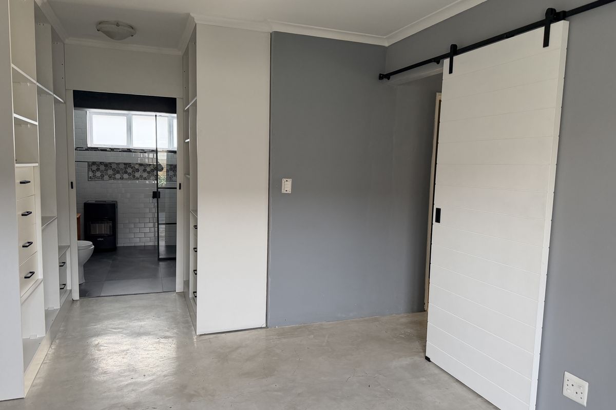 A spacious bedroom featuring polished concrete floors, built-in storage cabinetry, and a modern sliding barn door, with an adjoining bathroom visible.