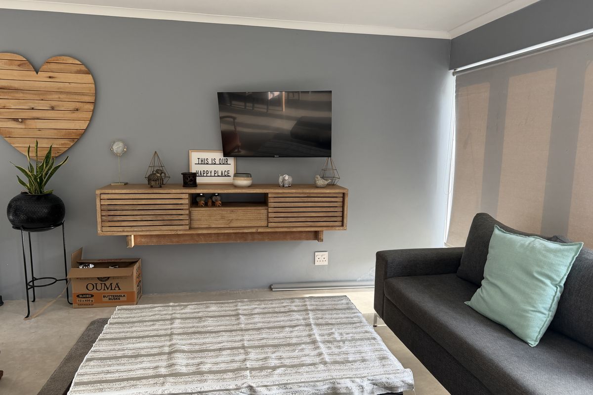 A well-maintained living room featuring a modern floating timber media console, recessed downlighting, and neutral grey wall finishes.