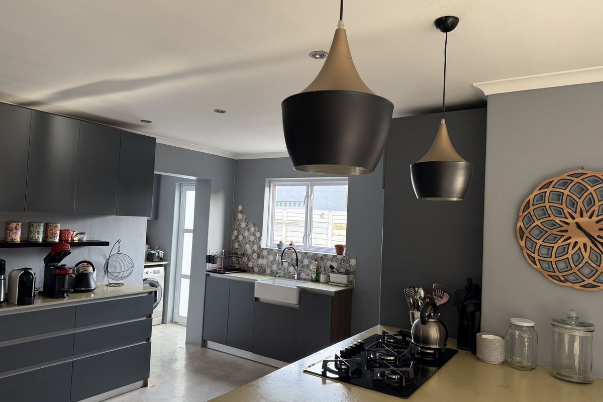 Modern kitchen featuring dark grey cabinetry, a gas cooktop, an apron-front sink, and stylish pendant lighting, with an adjacent laundry area.