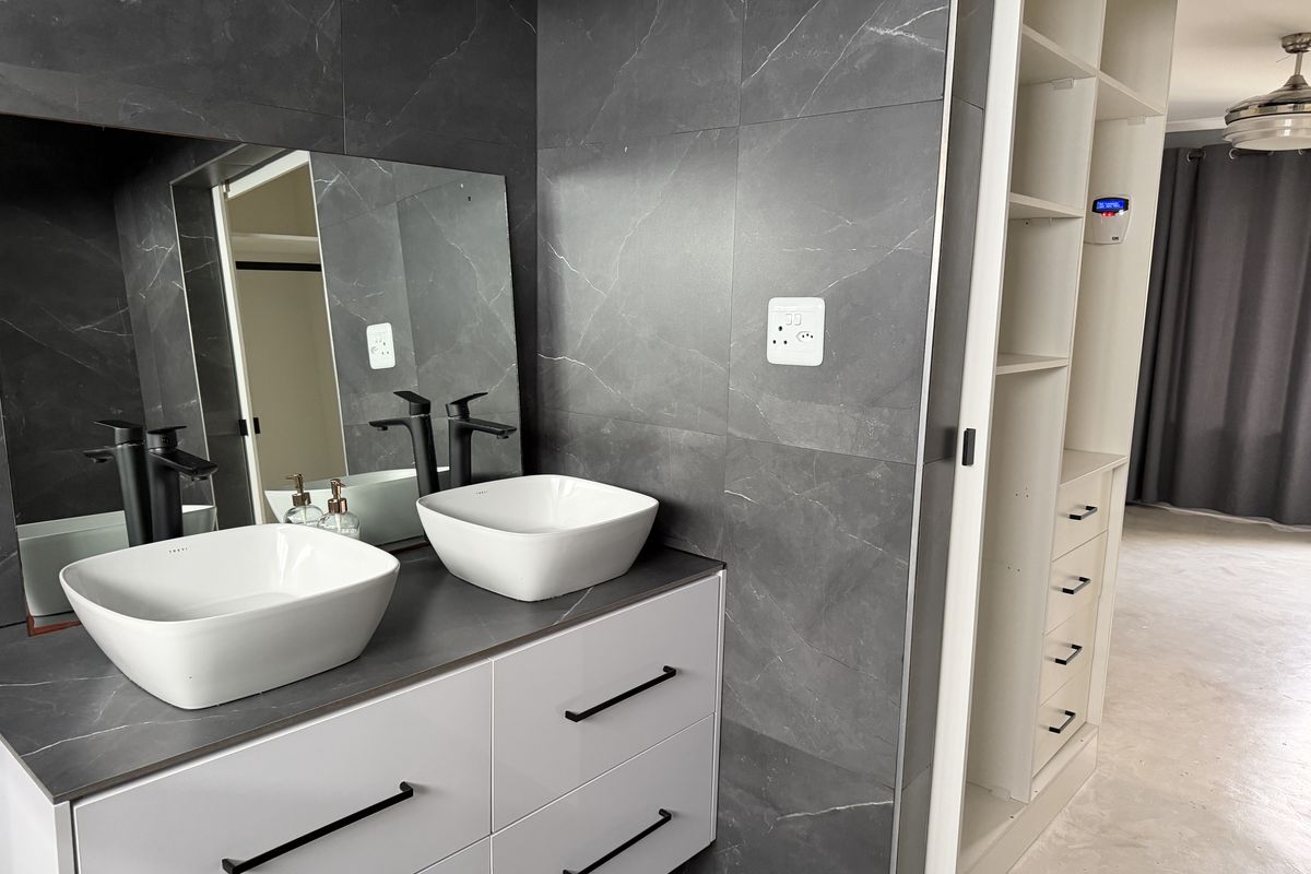 Modern bathroom featuring a double vanity with vessel sinks, matte black fixtures, and dark marble-look wall tiles, adjacent to built-in storage cabinetry.