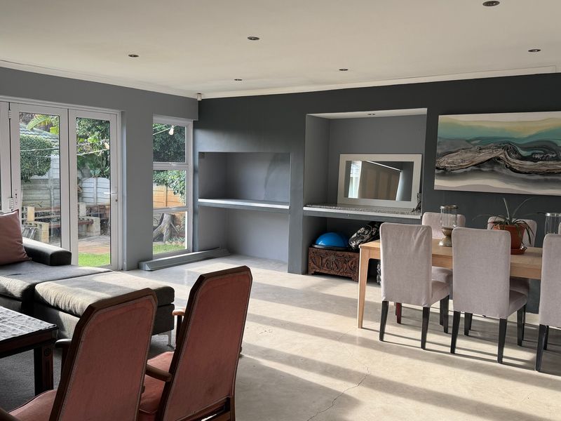 Spacious open-plan living and dining area featuring polished concrete floors, recessed lighting, a built-in fireplace, and direct access to the garden through french doors.