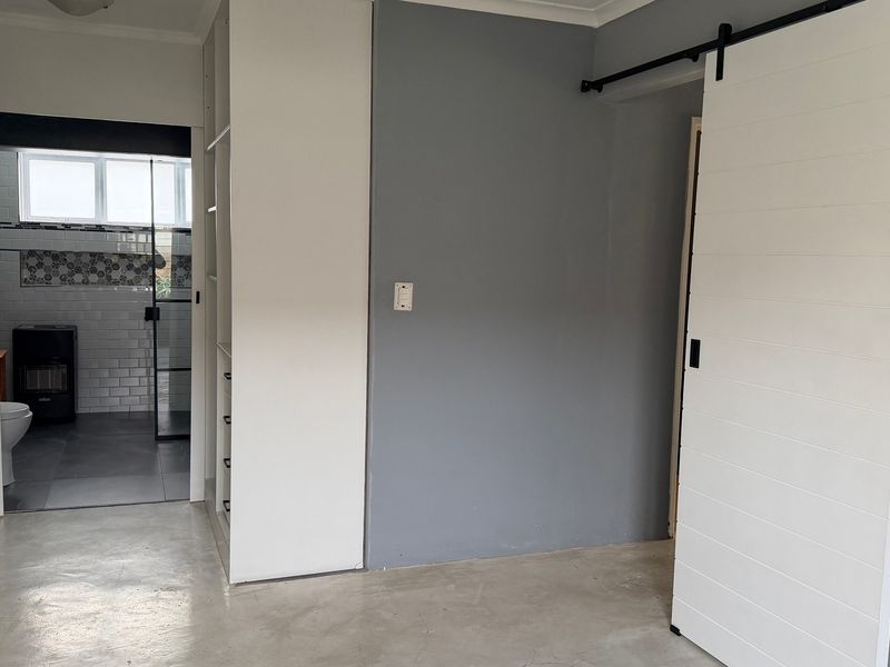 A spacious bedroom featuring polished concrete floors, built-in storage cabinetry, and a modern white sliding barn door leading to an en-suite bathroom.