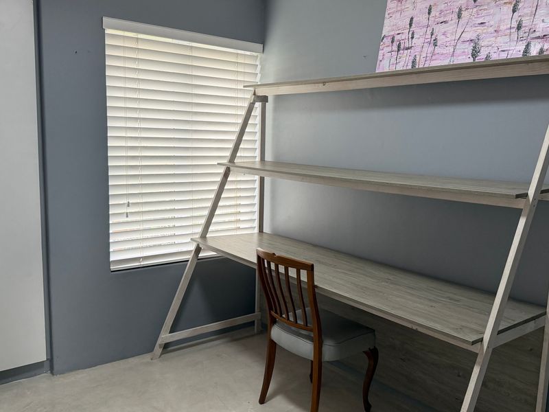 A bedroom featuring a built-in wardrobe, venetian blinds, and grey painted walls, providing a functional space for a home office or sleeping area.