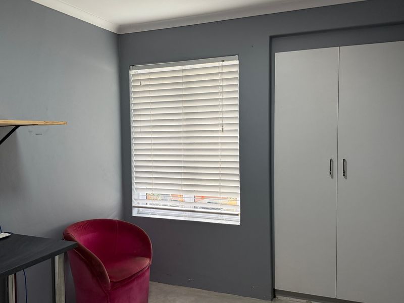 A bedroom featuring grey walls, a built-in wardrobe, and venetian blinds, providing a functional and neutral space.