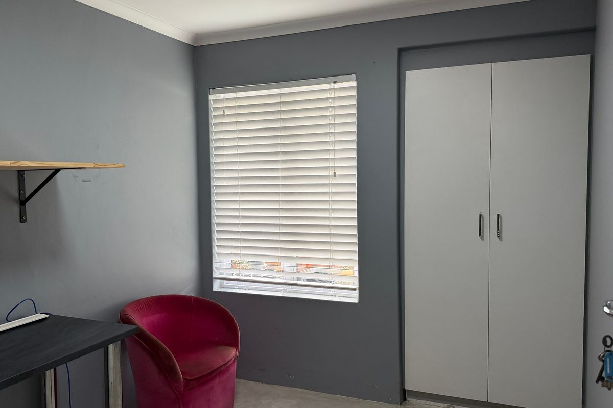 A bedroom featuring grey walls, a built-in wardrobe, and venetian blinds, providing a functional and neutral space.