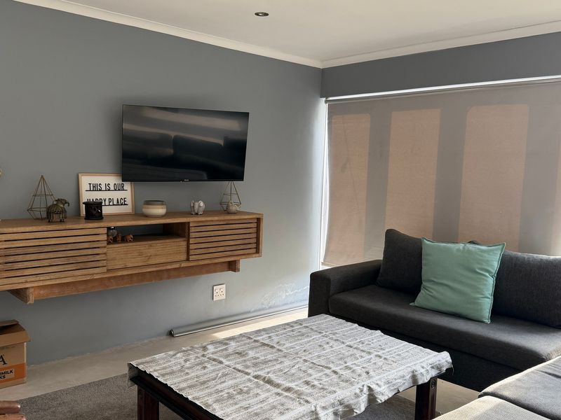 A living room featuring a wall-mounted timber media console, roller blinds, and recessed lighting, with visible wall dampness requiring attention.