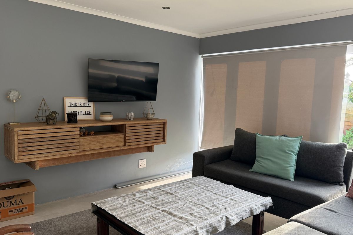 A living room featuring a wall-mounted timber media console, roller blinds, and recessed lighting, with visible wall dampness requiring attention.