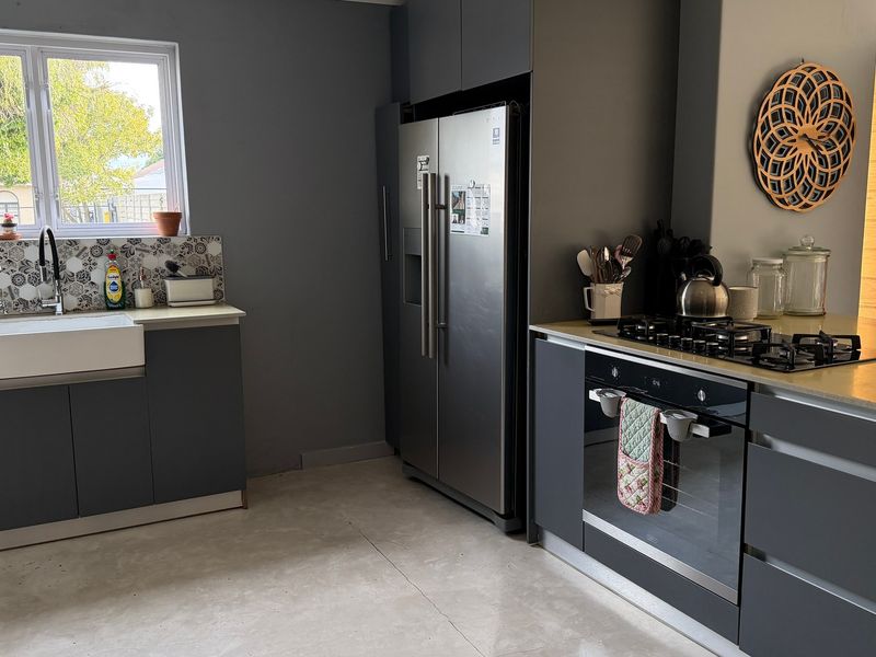 Modern kitchen featuring grey cabinetry, a farmhouse sink, patterned tile backsplash, gas hob, and built-in oven with stone countertops.