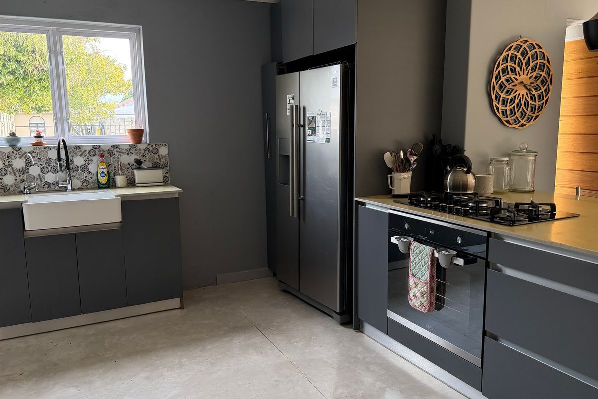 Modern kitchen featuring grey cabinetry, a farmhouse sink, patterned tile backsplash, gas hob, and built-in oven with stone countertops.