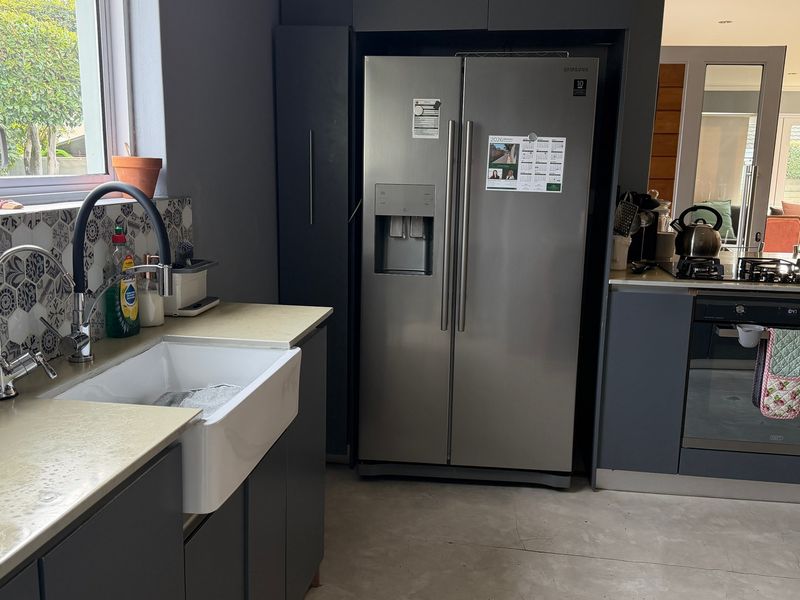 Modern kitchen featuring dark grey cabinetry, stone countertops, a farmhouse sink, and integrated appliances with a stylish patterned tile backsplash.