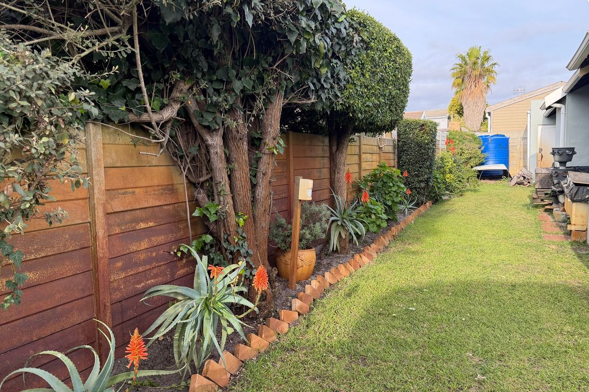 A side garden area featuring a lawn, established trees, brick edging, and a timber boundary fence with a rainwater tank at the rear.
