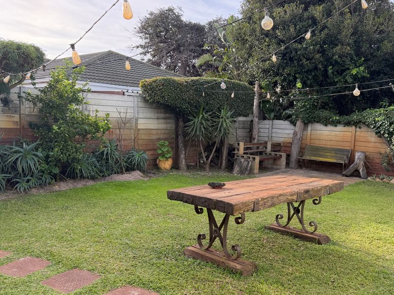A private backyard garden featuring a well-maintained lawn, paved stepping stones, and a perimeter boundary wall with mature landscaping.