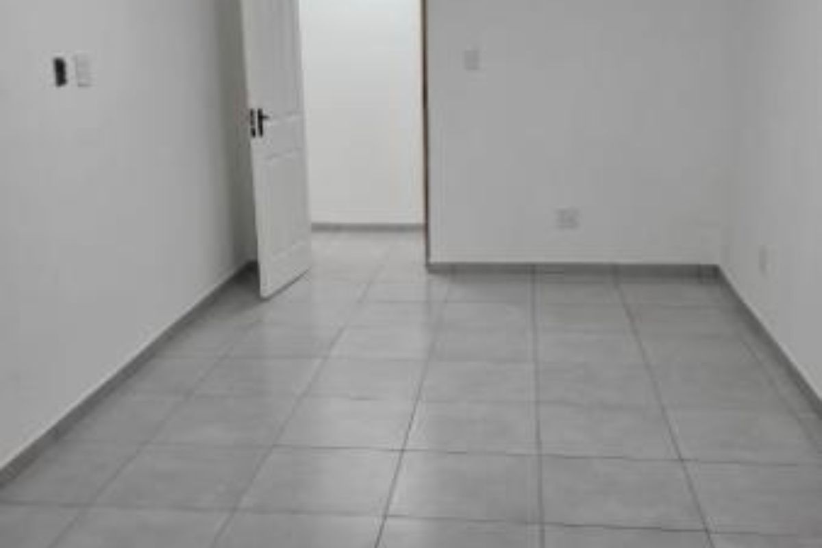A clean, empty living area featuring neutral tiled flooring and a simple ceiling light fixture, providing a blank canvas for interior design.