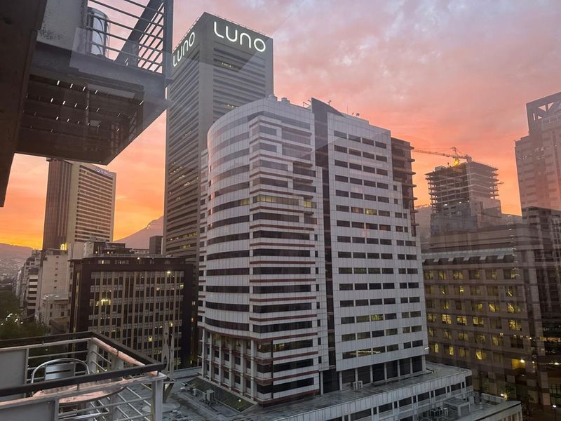 An elevated city skyline view at sunset, captured from a balcony overlooking surrounding high-rise commercial buildings.