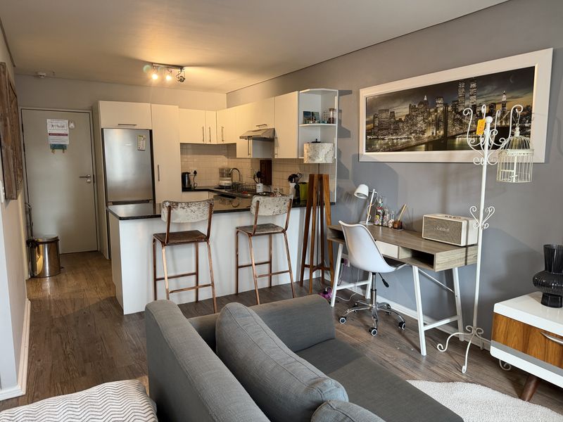 An open-plan living area featuring a modern kitchen with white cabinetry, stone countertops, and laminate flooring, seamlessly integrated with the living space.