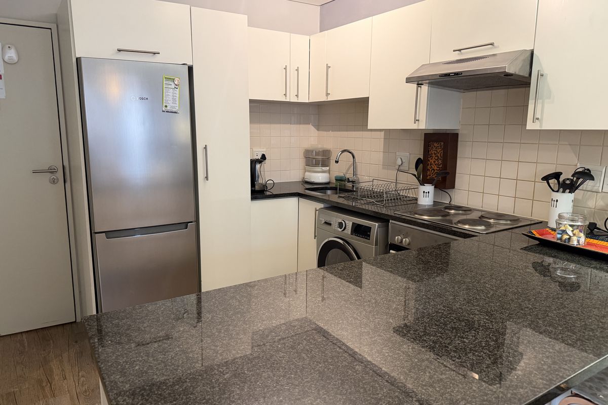 Compact kitchen featuring granite countertops, white cabinetry, stainless steel appliances, and a tiled backsplash, offering a functional and efficient workspace.