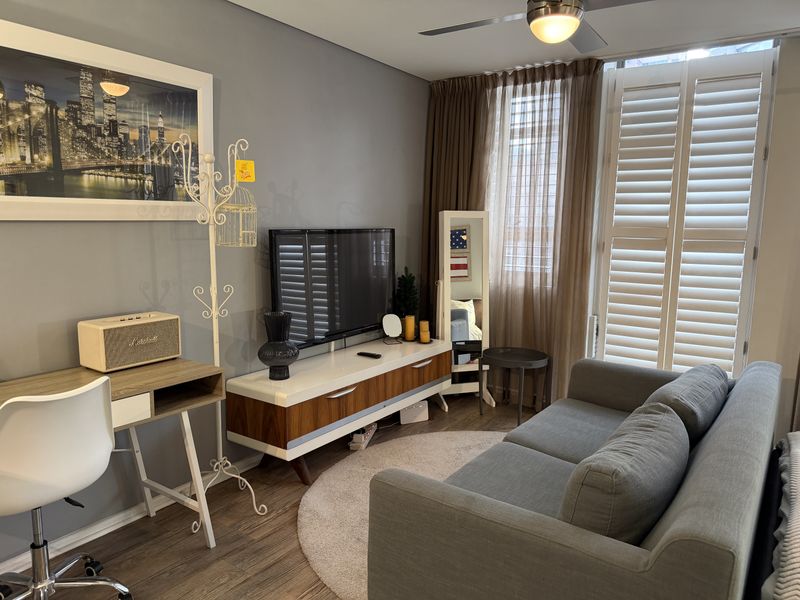 A well-maintained living room featuring laminate flooring, a ceiling fan, and plantation shutters that provide excellent natural light control.
