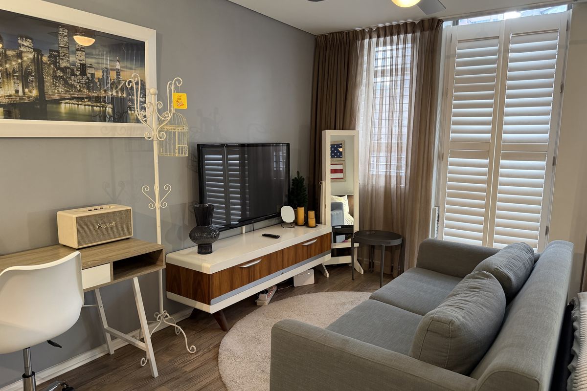 A well-maintained living room featuring laminate flooring, a ceiling fan, and plantation shutters that provide excellent natural light control.