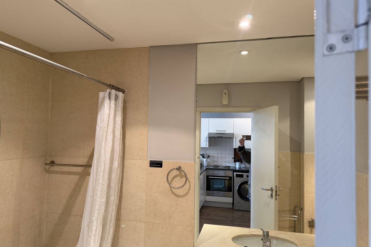 A clean bathroom featuring tiled walls, a shower with a curtain, and a vanity basin with a large wall mirror.