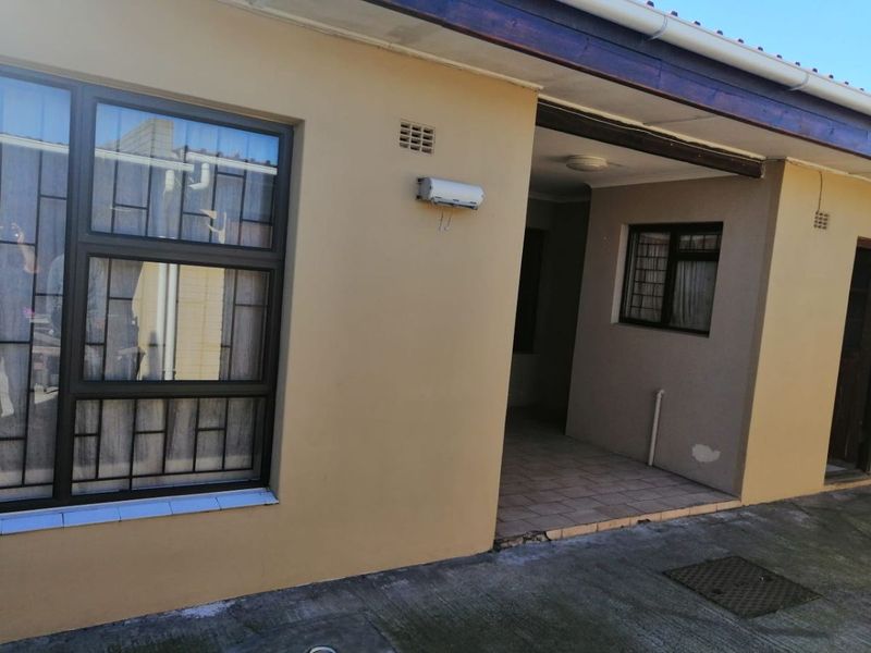 Rear exterior view of the flat featuring a small tiled patio area, aluminium window frames with security bars, and concrete paving.