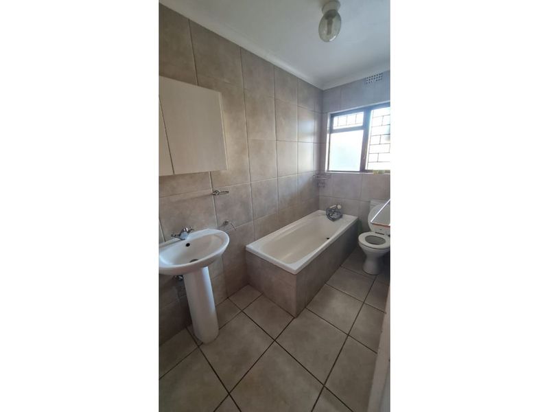 A functional bathroom featuring a pedestal basin, built-in bathtub, and toilet with neutral wall and floor tiling.