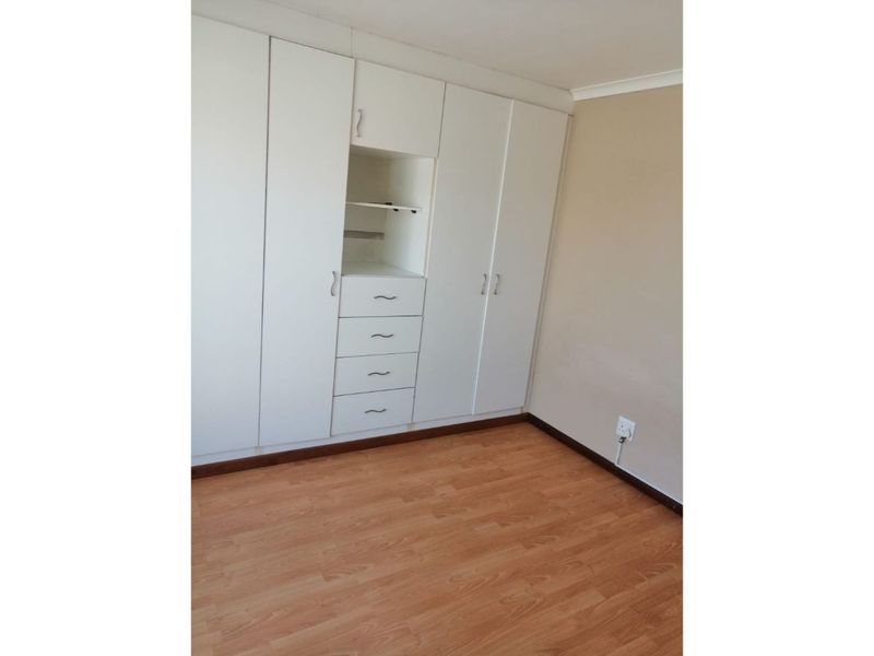 A clean, empty bedroom featuring light-toned laminate flooring and extensive white built-in cupboards with integrated shelving and drawers.