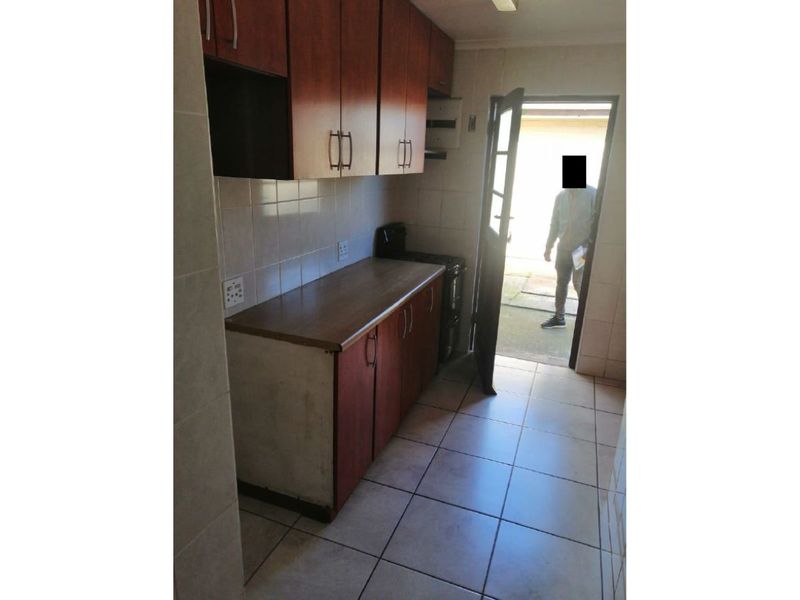 A compact kitchen featuring built-in wooden cabinetry, tiled flooring, and direct access to the exterior.