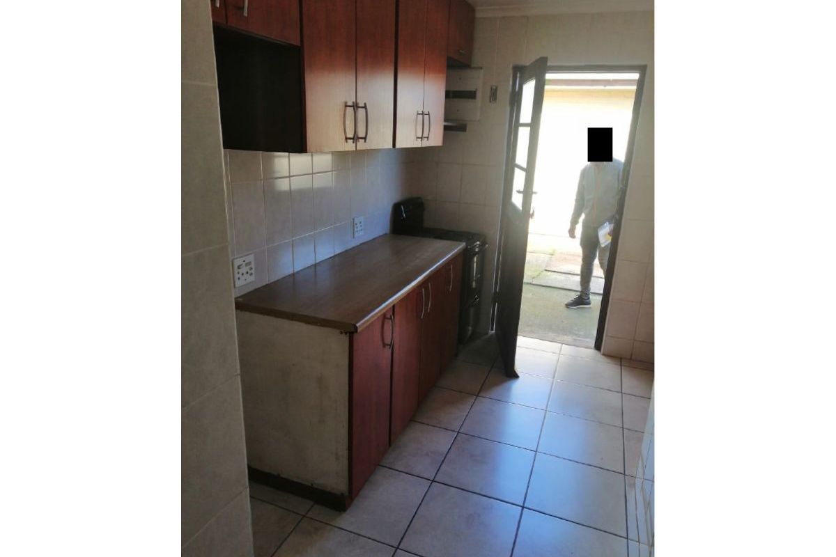 A compact kitchen featuring built-in wooden cabinetry, tiled flooring, and direct access to the exterior.