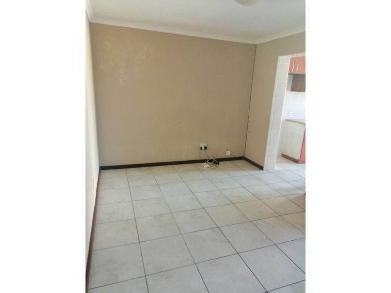 An empty living area featuring neutral ceramic floor tiles, coved ceiling cornices, and direct access to the adjacent kitchen space.