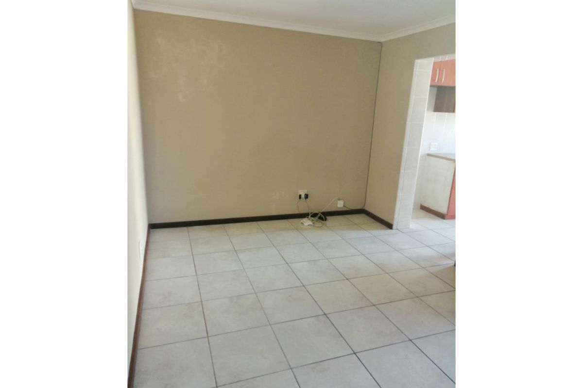An empty living area featuring neutral ceramic floor tiles, coved ceiling cornices, and direct access to the adjacent kitchen space.