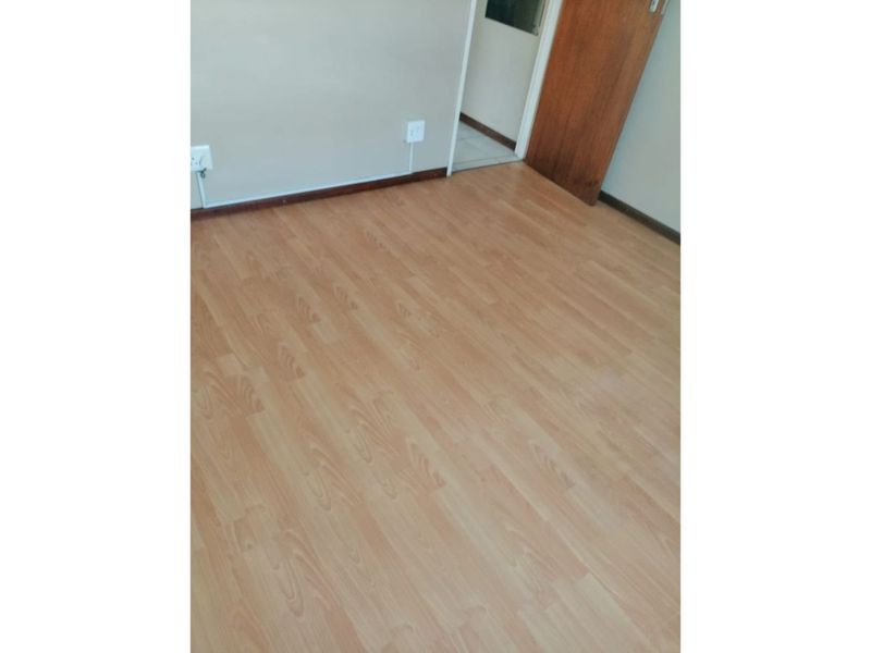 An empty bedroom featuring light-toned laminate flooring, neutral walls, and a wooden door leading to an adjacent space.