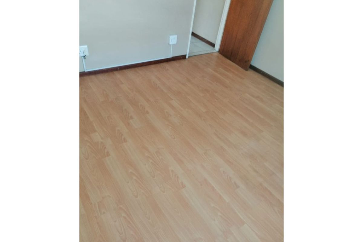 An empty bedroom featuring light-toned laminate flooring, neutral walls, and a wooden door leading to an adjacent space.