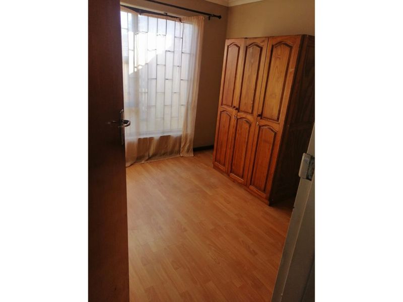 A bedroom featuring laminate flooring, a window with security bars, and a curtain rod, viewed from the doorway.