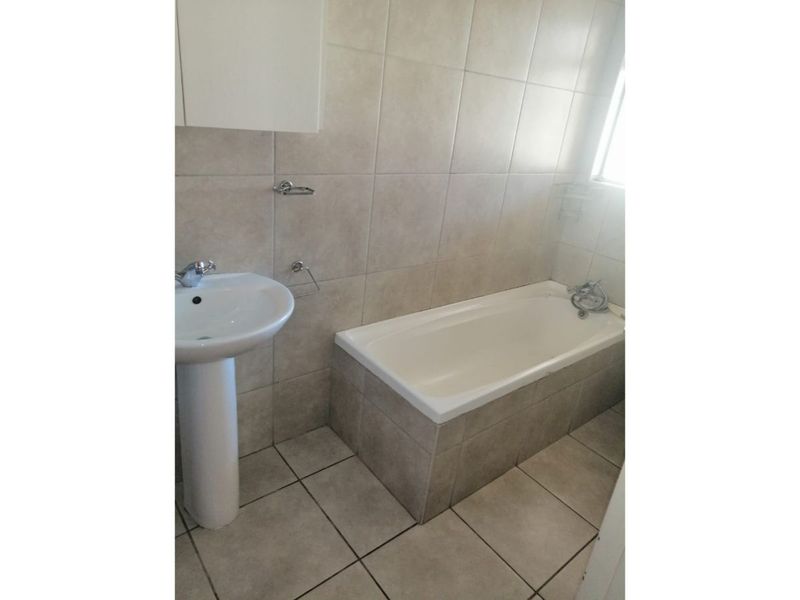 A functional bathroom featuring a pedestal basin, bathtub, and neutral wall and floor tiling.