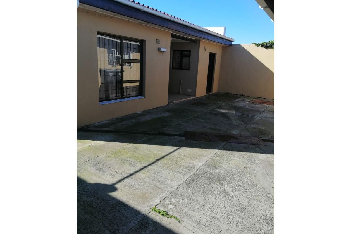 Rear exterior view of the property featuring a concrete paved courtyard area with security bars on windows and perimeter walling.