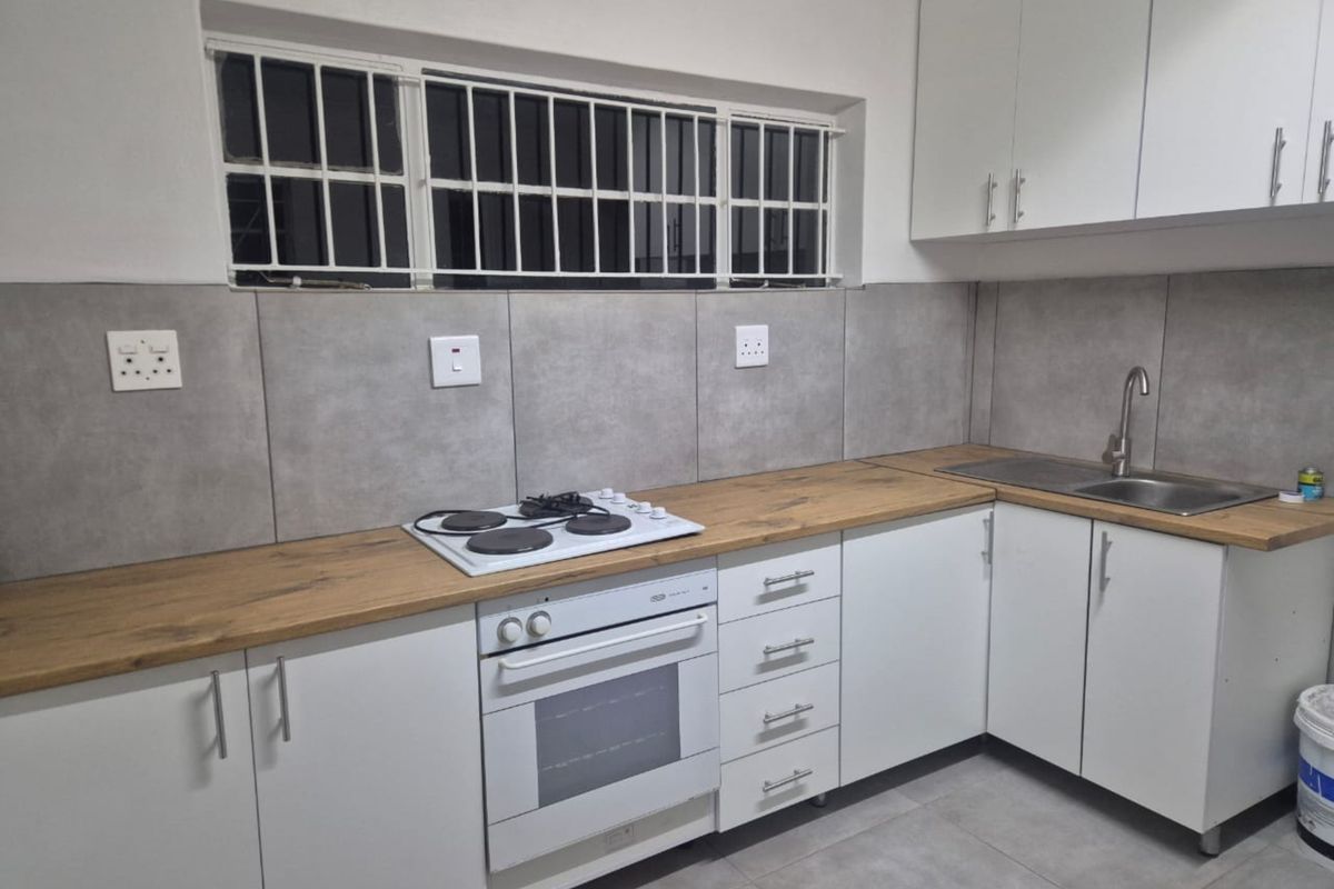 A clean, modern kitchen featuring white cabinetry, wood-look laminate countertops, a built-in oven and hob, and grey tiled splashbacks.