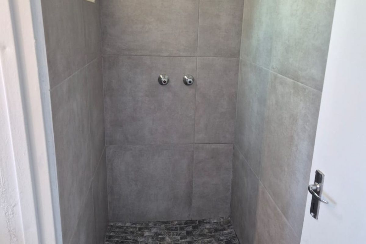 A modern walk-in shower featuring grey large-format wall tiles and a textured stone-look tiled floor with a fixed shower head and mixer.