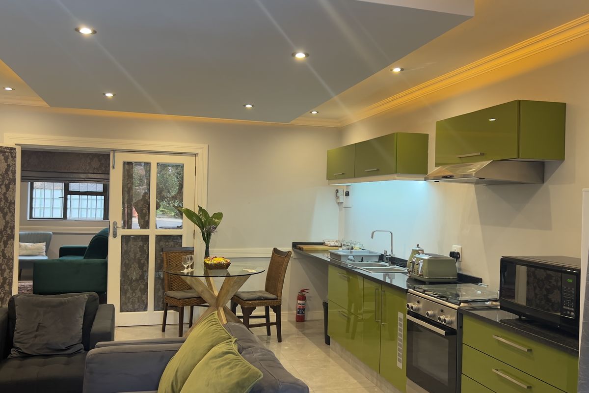 Open-plan living area featuring a modern kitchen with gloss green cabinetry, stone countertops, integrated appliances, and recessed ceiling lighting with ambient cove accents.