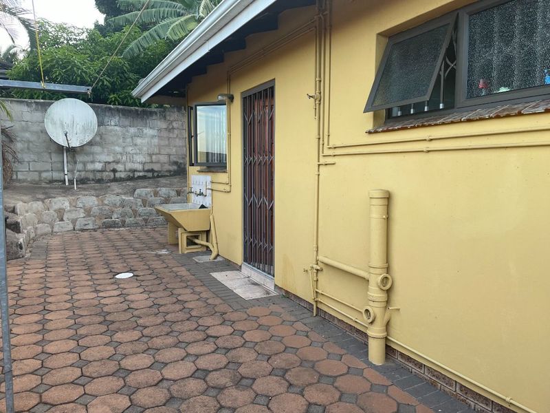 Rear exterior view of the cottage featuring a paved patio area, external utility sink, and security gate access.