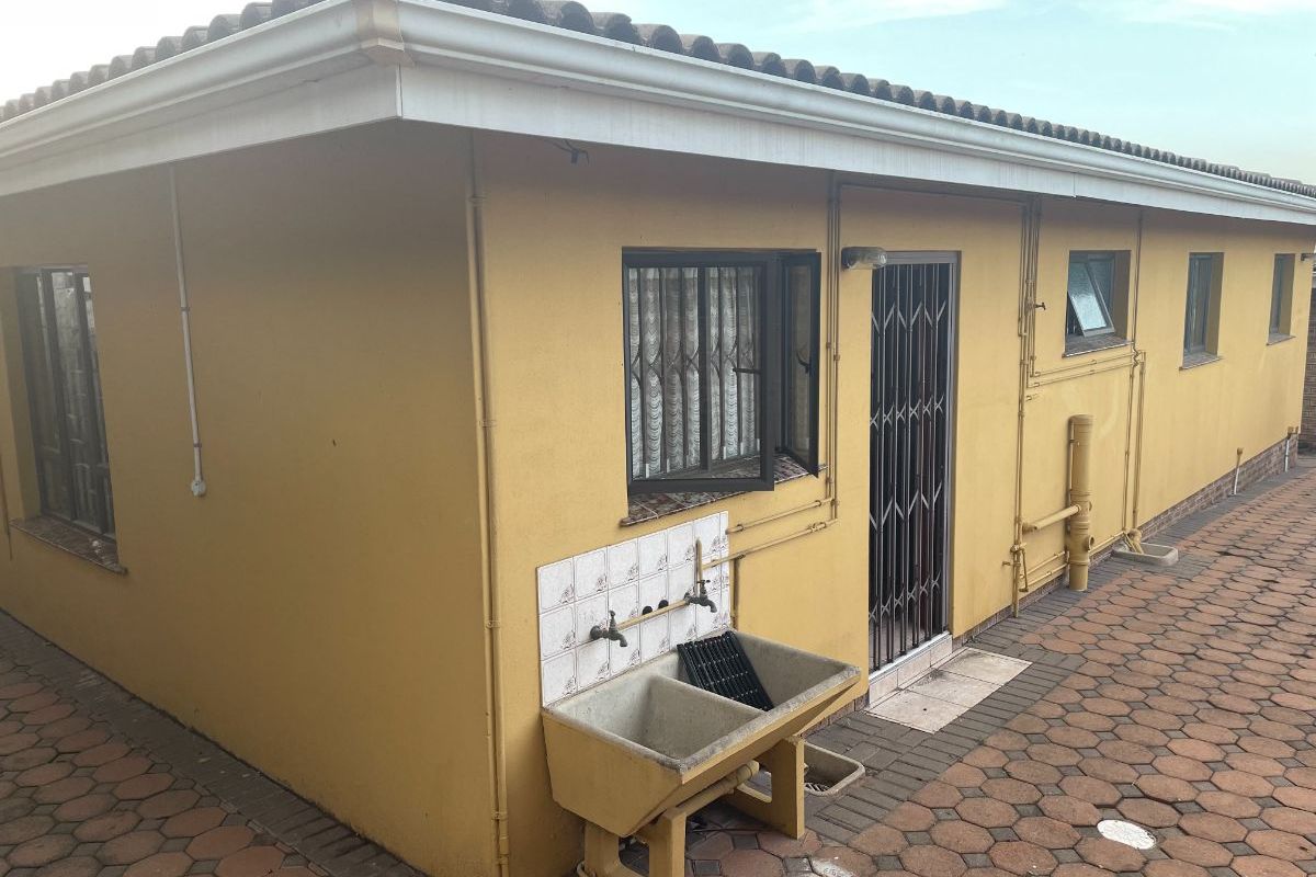Rear exterior view of the cottage featuring a paved patio area, external laundry trough, and security gate access.