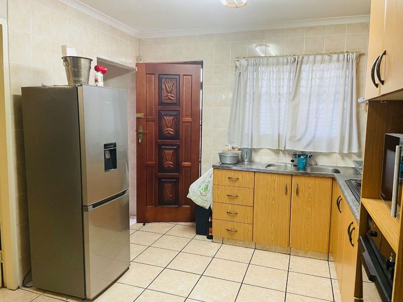 A functional kitchen featuring laminate cabinetry, tiled splashbacks, tiled flooring, and a solid timber door leading to the exterior.