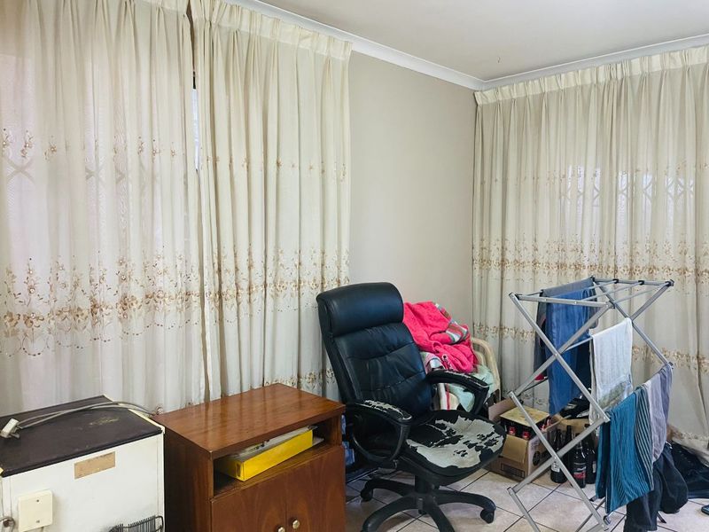 A living area featuring tiled flooring and neutral walls, currently utilized as a multi-purpose space with window treatments.